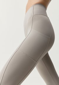 Těsně přiléhající leg�íny vyrobené z měkké, pružné tkaniny ve světle béžové barvě, s plochými švy a vysokým pasem pro hladký siluetu.