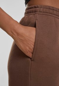 Bruine joggingbroek met een elastische tailleband, zijzak en zachte textuur. Close-up weergave met een hand in de zak.