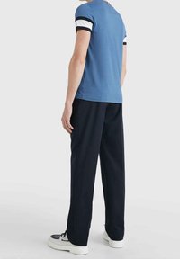 Camiseta de manga corta azul con acentos a rayas en blanco y negro contrastantes en las mangas, combinada con pantalones negros y zapatillas de suela blanca.
