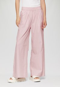 Pantalons à larges jambes rayés roses et blancs avec une taille élastique, en tissu léger et à coupe décontractée. Présentés avec des sandales blanches chunky.