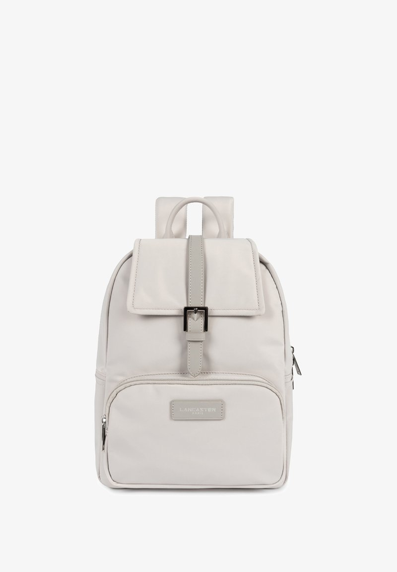 Light grey backpack with adjustable straps, a flap closure, front zip pocket, and a smooth, textured finish. Features brand logo on the front.