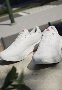 Białe sportowe buty z oddychającą siateczką na górze, fakturowaną powierzchnią, różowymi akcentami oraz wyściełaną podeszwą z lekko podniesionym obcasem.