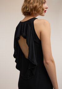 Vestito nero con schiena drappeggiata e apertura a goccia. Decorato con perline lungo le rouches, realizzato in un tessuto liscio.