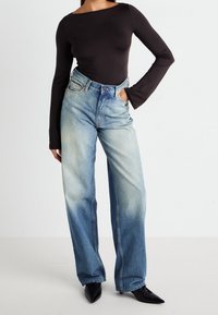 Body a maniche lunghe nera abbinata a jeans a vita alta blu chiaro a gamba larga, con una texture sbiadita. Indossato con scarpe nere a punta.