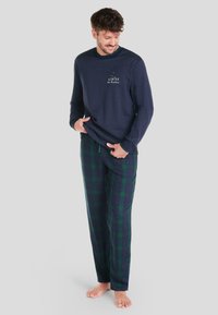 Camisa de manga larga de color navy con estampado "INVIERNO" y pantalones de pijama informales a cuadros en verde oscuro y azul con patrón de cuadros grandes.