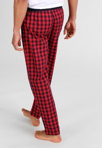 Pantalones de pijama a cuadros rojos y azul marino con cinturilla elástica, corte recto y material de algodón suave, mostrados desde un ángulo lateral.