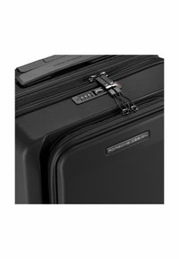 Maleta rígida negra con superficie texturizada, cremalleras dobles, mecanismo de cierre y placa con marca distintiva. Presenta un diseño aerodinámico.