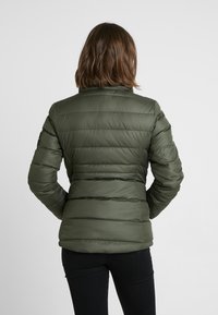 Veste matelassée verte avec un col haut, présentant des sections horizontales matelassées et une texture lisse et brillante. Aucun détail matériel visible.