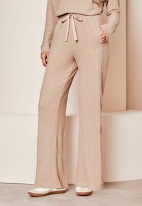Beige hladké pletené kalhoty s elastickým páskem a širokými nohavicemi. Disponují bočními kapsami a měkkou texturou pro pohodlí.