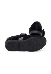 Zapatos de ante negro con una correa de charol brillante. La suela es de goma texturizada con patrones florales y de corazones.