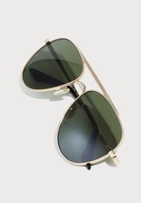 Occhiali da sole in stile aviator con lenti verde scuro, montatura in metallo dorato e accenti neri sugli steli. Le lenti sono leggermente specchiate.