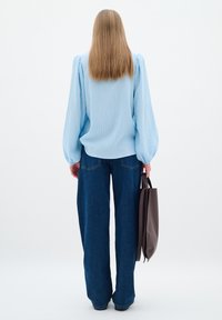 Ljusblå blus med puffärmar, tillsammans med lösa mörkblå denimjeans. Håller en brun toteväska. Ren, minimalistisk stil.