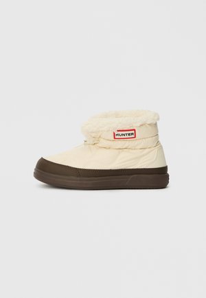 Bottes de cheville isolées crème et marron avec doublure en polaire et patch logo Hunter sur le côté, chaussures d'hiver pour temps froid.