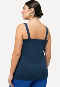 Tmavě modrý top s širšími ramínky a přiléhavým střihem. Vyrobený z měkké látky, s čistým výstřihem a hladkou texturou.
