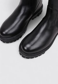 Bottines en cuir noir avec une finition lisse, bout rond et semelle en caoutchouc épaisse avec une texture antidérapante. Panneaux élastiques sur les côtés inclus.