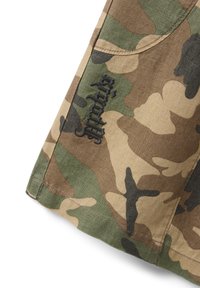 Section of fabric with green, brown, tan, and black camouflage pattern and black embroidered text in stylized font on the surface.