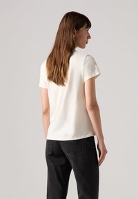 Weißes T-Shirt mit kurzen Ärmeln und Rundhalsausschnitt in glatter Textur, kombiniert mit schwarzer, hochtaillierter Jeans mit Gesäßtaschen.