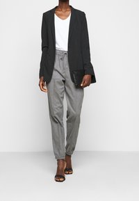 Czarna marynarka na białej koszulce z dekoltem w serek, w połączeniu z jasnoszarymi spodniami na sznurki i czarnymi sandałami na obcasie. Prosta kopertówka w ręku.