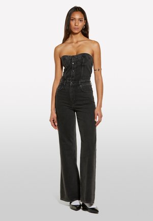 Combinaison en denim noir avec un design sans bretelles, un bouton sur le devant, taille haute et coupe large. Texture lisse avec des détails de coutures subtiles.