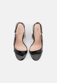 Paire d'escarpins à talons ouverts en cuir verni noir, avec bride arrière à boucle à la cheville et semelles intérieures beiges affichant le nom de la marque "RAID".