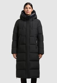 Manteau noir long en doudoune avec capuche, présentant un design matelassé, deux poches latérales et un cordon de serrage au cou. Texture lisse, silhouette épurée.