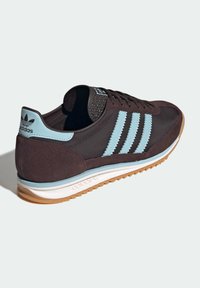 Black and blue athletic sneakers with three distinctive light blue stripes, suede and textile upper, rubber sole, and textured tongue.