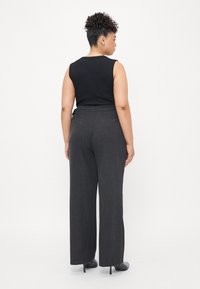 Schwarzes ärmelloses Oberteil, kombiniert mit grauen weiten Hosen. Der Stoff wirkt glatt. Einfaches Design ohne sichtbare Muster oder Hardwaredetails.