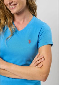 Lichtblauw katoenen V-hals t-shirt met korte mouwen en een klein rood logo op de linkerborst. Vlakte textuur, casual ontwerp.