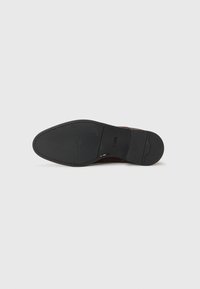 Suela de zapato de cuero marrón con una suela exterior de goma negra lisa. Presenta un logotipo sutil y una forma redondeada con un patrón de relieve mínimo.