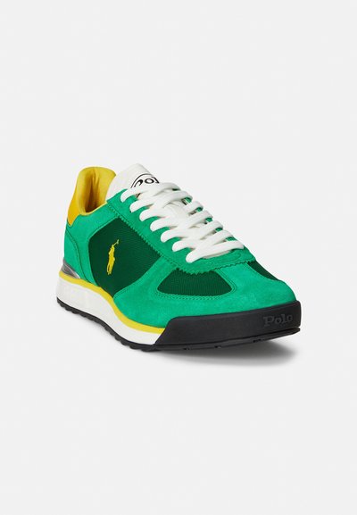 Green and yellow athletic sneaker with suede and mesh materials, white laces, black sole, and white accents. Features a logo on the tongue.