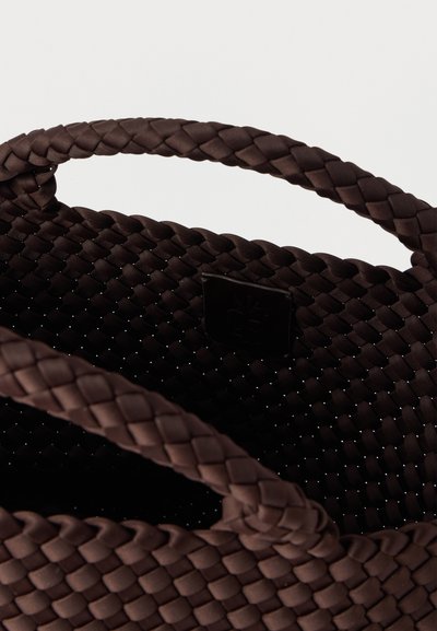 Καφέ υφαντή τσάντα χειρός με υφή μοτίβου, με δύο πλεκτές λαβές και μικρή ανάγλυφη ετικέτα με λογότυπο στο εσωτερικό.