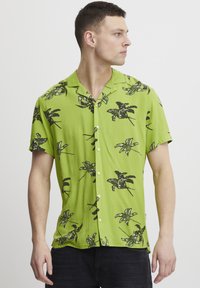 Camisa verde de manga corta con estampado de hojas tropicales negras, diseño con cuello, tejido ligero y cierre de botones en la parte delantera.