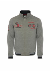 Siva dukserica na zip s visokim ovratnikom, rebrastim manžetama i donjim rubom, koja sadrži crvene izvezene logotipe i zakrpe na prsima i rukavima.