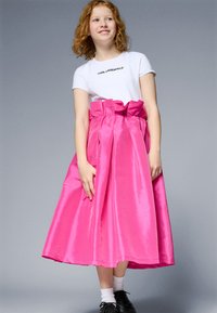 Bright pink satin skirt with a structured waistband and bow detail. Worn with a white short-sleeve shirt featuring black lettering.