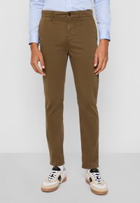 Chinos de algodón marrones con corte recto, que cuentan con un cierre de botón y bolsillos delanteros, combinados con zapatillas blancas y marrones.