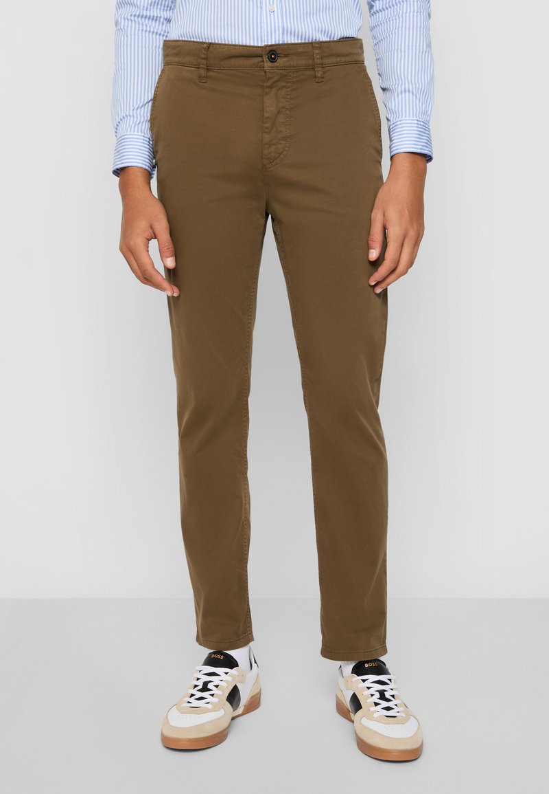 Chinos de algodón marrones con corte recto, que cuentan con un cierre de botón y bolsillos delanteros, combinados con zapatillas blancas y marrones.