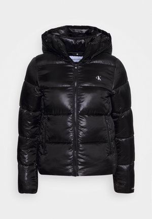Doudoune noire brillante avec capuche, fermeture éclair à l'avant, poches latérales zippées et petit logo blanc "cK" sur la poitrine et le bord de la manche.