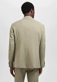 Beige colbert met een getailleerde pasvorm, enkele split aan de achterkant en knoopsluiting op de mouwen. Soepele textuur en minimalistisch ontwerp.