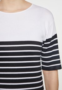 Korte mouw shirt van gebreide stof met een wit bovenstuk en horizontale zwart-witte strepen op de onderste helft.