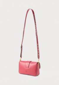 Rdeča usnjena torbica čez ramo s ukrivljeno obliko, z zlatim okovjem in podrobno naramnico, ki vključuje kovinske zakovice in gladek dokončanje.