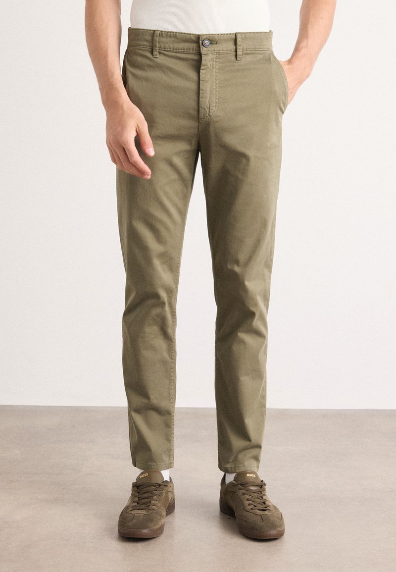 Chinos kaki en coton, présentant une coupe ajustée, des poches latérales, une fermeture à bouton, et des détails de couture discrets, associés à des sneakers marron.