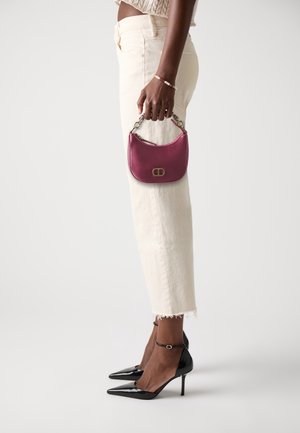 Sac à main en satin magenta avec une forme courbée, des accessoires dorés et une courte bandoulière en chaîne, assorti à un jean blanc raccourci et des escarpins noirs.