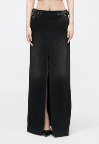 Fekete denim maxiszoknya elülső hasítékkal, két oldalsó zsebbel és díszes csatokkal a derékrészen. Simább textúrával és testhezálló fazonnal.