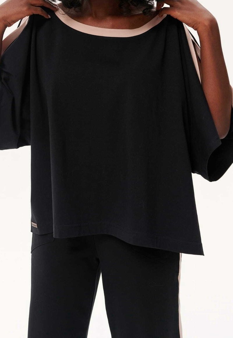 Haut noir oversize avec un col rond orné d'un biais beige contrastant. Confectionné dans un tissu doux avec une coupe ample, idéal pour superposer.