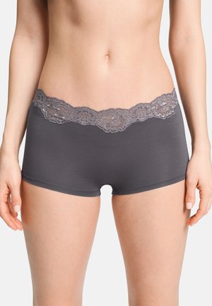 Vrouw draagt donkergrijze boyshort onderbroek met kanten randje aan de taille, zichtbaar van taille tot bovenbenen tegen een effen achtergrond.