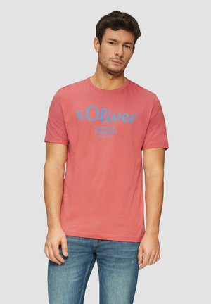 Rode T-shirt met korte mouwen en ronde hals, voorzien van een blauwe bedrukte merklogo en tekst op de voorkant, gedragen met blauwe spijkerbroek.