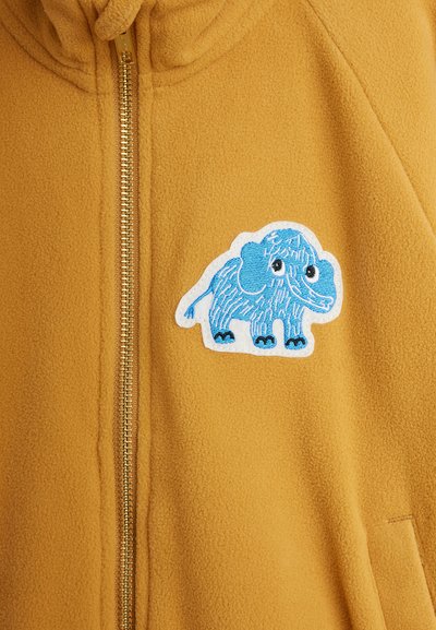 Senfgelb Fleecejacke mit Frontreißverschluss und einem blauen Cartoon-Elefanten-Patch auf der rechten Brustseite.