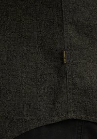 Mørkt mønsteret stof med et geometrisk design, der har et label i gult med påskriften "PME Legend." Teksturen ser glat og let ud.
