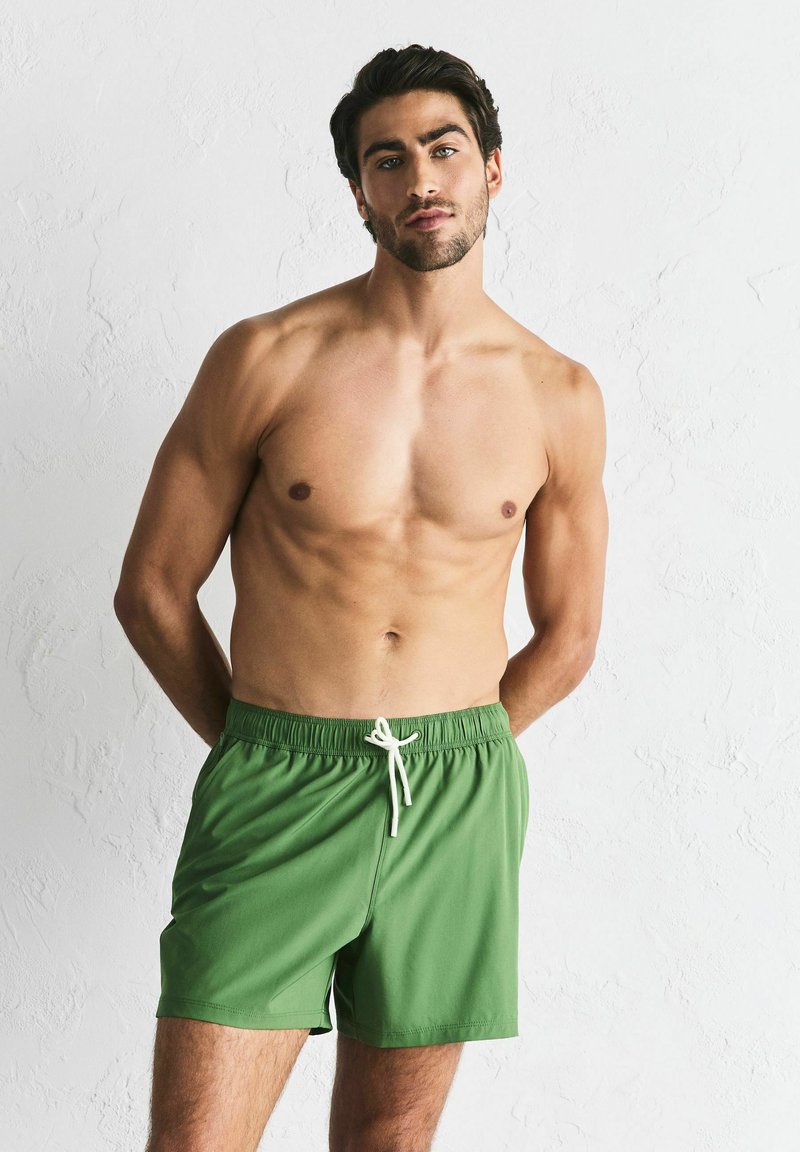 Shorts de bain verts à texture douce, avec une ceinture élastique et un cordon blanc. Coupe courte, design uni, adapté pour la plage.