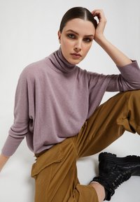 Jasnoliliowa sweter z golfem o luźnym kroju i rypsowym wykończeniu, połączony z brązowymi spodniami cargo i czarnymi sznurowanymi botkami za kostkę.